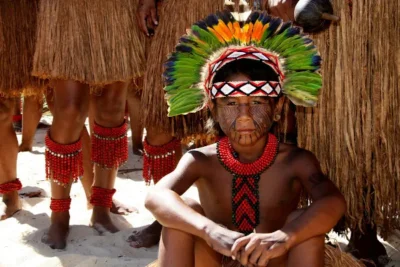 crianca do povo indigena brasileiro pataxo sentada com cocar na cabeca e colares tipicos de sua cultura