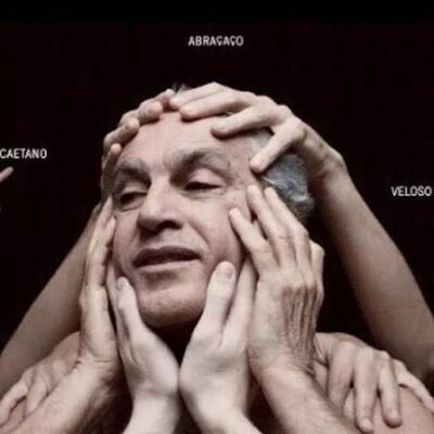 Caetano Veloso aparece em primeiro plano, com os olhos semicerrados e expressão serena. Diversas mãos tocam delicadamente seu rosto e cabeça, em gesto de acolhimento. Ao fundo, fundo preto e as palavras "Abraçaço", "Caetano" e "Veloso" aparecem distribuídas na imagem.