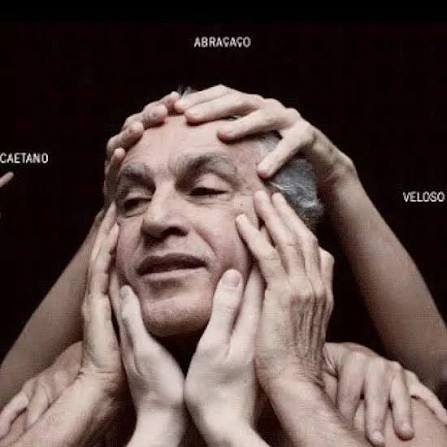 Caetano Veloso aparece em primeiro plano, com os olhos semicerrados e expressão serena. Diversas mãos tocam delicadamente seu rosto e cabeça, em gesto de acolhimento. Ao fundo, fundo preto e as palavras "Abraçaço", "Caetano" e "Veloso" aparecem distribuídas na imagem.