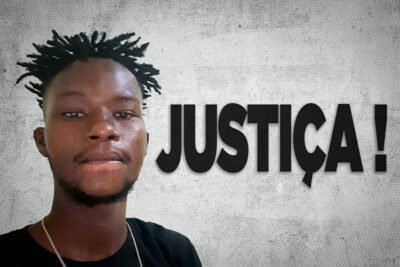 Retrato de um jovem negro com cabelos curtos em dreadlocks, barba rala e camiseta preta. Ao lado da fotografia, a palavra "JUSTIÇA!" aparece em destaque sobre um fundo cinza texturizado.