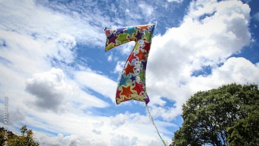 Low Angle View Of Colorful Number 7 Helium Balloon Against Cloudy Sky