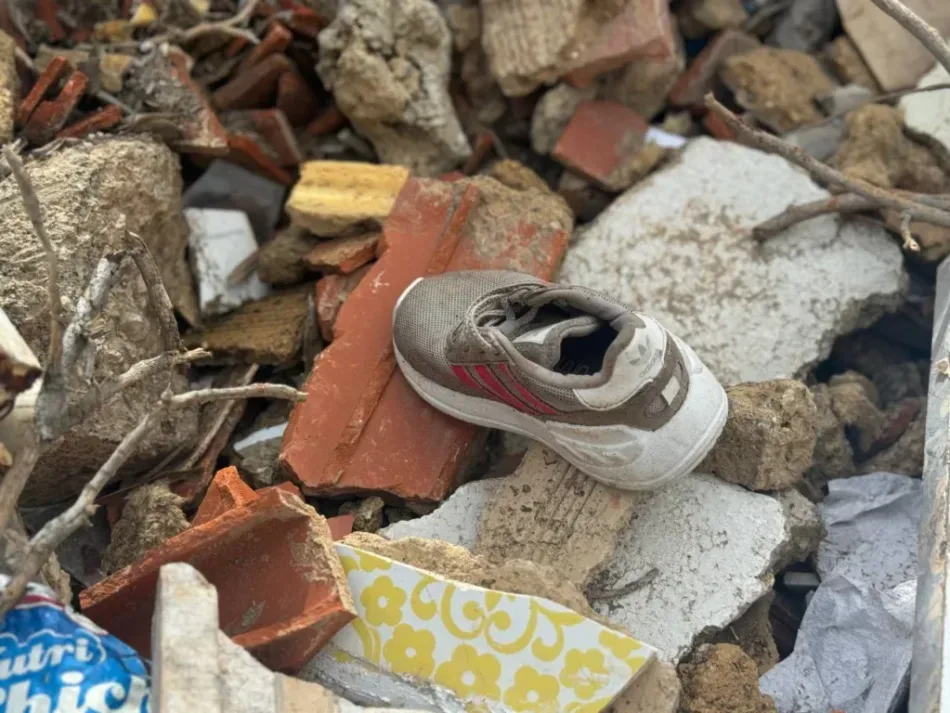 Em meio aos escombros de uma construção, um tênis cinza repousa sobre pedaços de concreto, tijolos e telhas quebradas. A cena destaca os vestígios da destruição e sugere a perda causada pelo desastre.