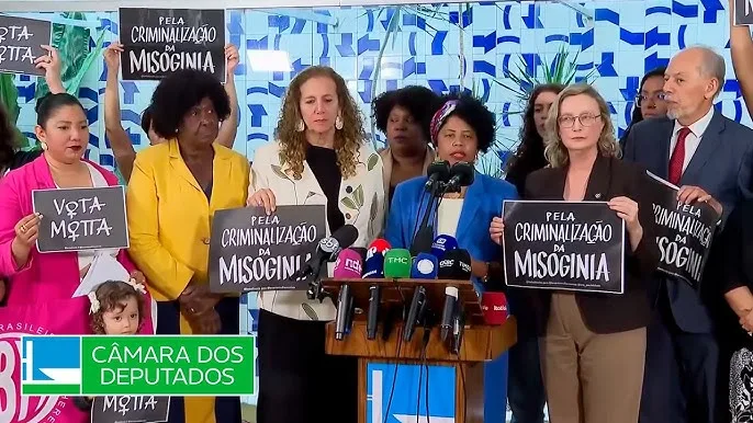 Parlamentares, em sua maioria mulheres, participam de uma coletiva de imprensa na Câmara dos Deputados. Elas seguram cartazes com a frase "Chega de cumplicidade com a misoginia" diante de microfones.